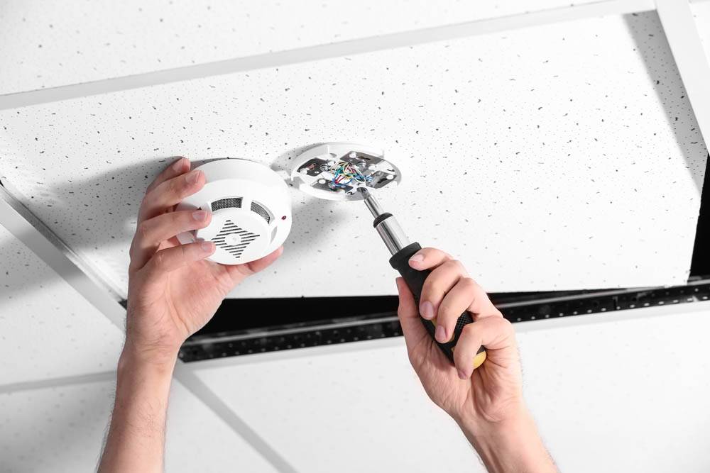 Young male technician installing smoke alarm system indoors